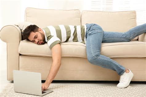 Lazy Young Man Using Laptop While Lying On Sofa At Home Stock Photo