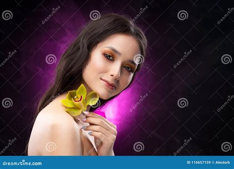 A Beautiful Brunette Nude Shoulders Girl Sensually Holds A Flower Of An Orchid In Her Hands