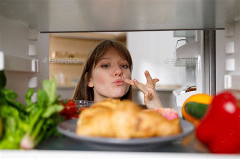 Girl Opened The Refrigerator And Looks At The Pastry Food And Tastes It Licking Her Fingers