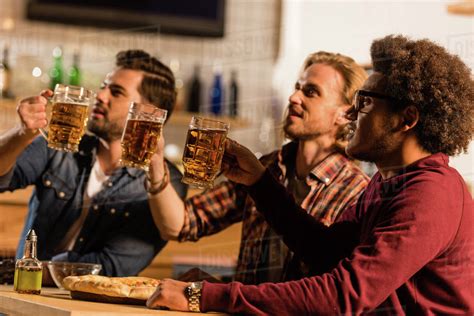 Handsome Young Multiethnic Men Drinking Beer And Looking Away In Bar