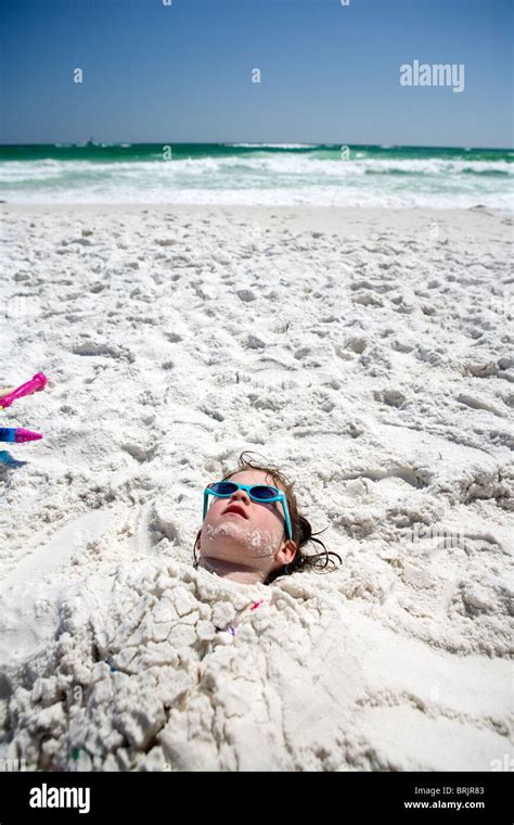 A Little Girl Is Buried In The Sand Up To Her Head At The Beach With