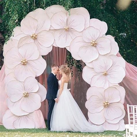 A Bride And Groom Standing In Front Of A Giant Flower Arch