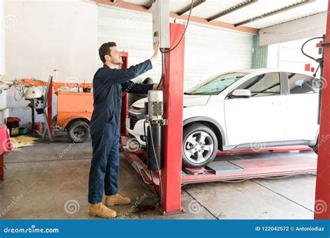Car Mechanic Operating Hydraulic Lift In Repair Shop Stock Photo