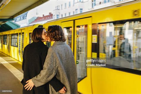 Lesbian Couple Kissing While Standing By Yellow Train At Railroad