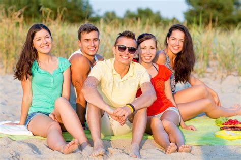 Amigos Sonrientes Que Se Sientan En La Playa Del Verano Imagen De