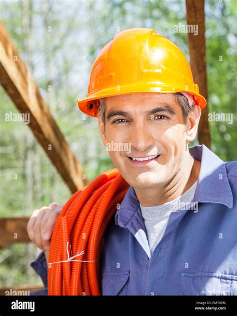 Smiling Construction Worker Carrying Rolled Pipe At Site Stock Photo