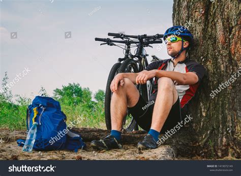 Male Mountain Biker Resting On Bike Ride Sitting On Ground Under A