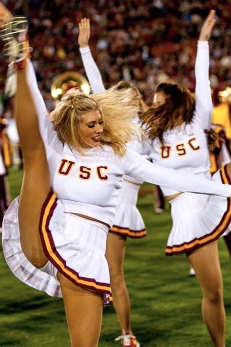 Two Cheerleaders In White Uniforms Are Dancing On The Field At A Football Game