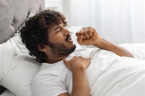 Sick Indian Man Lying In Bed Coughing And Touching Chest Stock Image