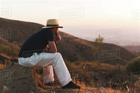 Thoughtful Man Looking Away While Sitting On Rock Against Clear Sky And