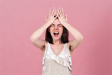Young Brunette Woman In A Rage Screams Opening Her Mouth Wide And Pressing Her Palms To Her
