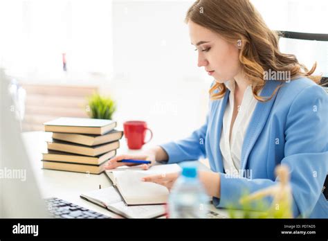 Beautiful Young Girl Sitting At Desk In Office Holding A Pen In Her