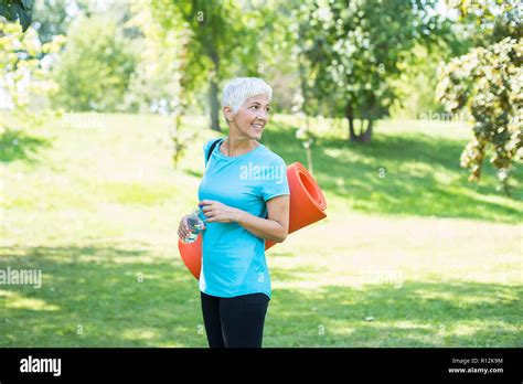Portrait Of Senior Woman Holds Fitness Mat On Her Back In The Park And