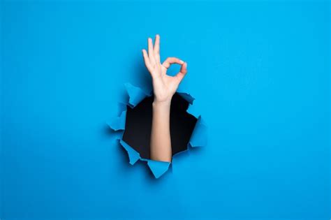 Free Photo Close Up Of Woman Hand With Okay Gesture Through Blue Hole