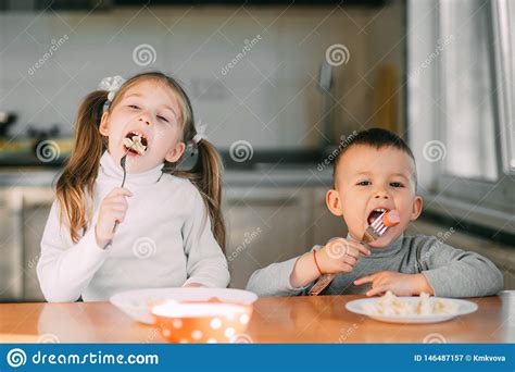 Boy And Girl Children In The Kitchen Eating Sausages With Pasta Is Very