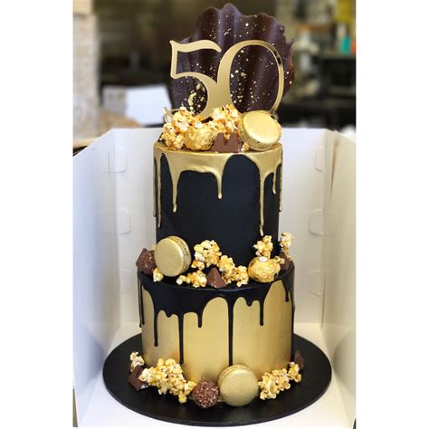black and gold two tier with caramel popcorn macarons chocolate drip and custom cake topper