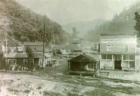 An Old Black And White Photo Of A Train Station In The Middle Of Town