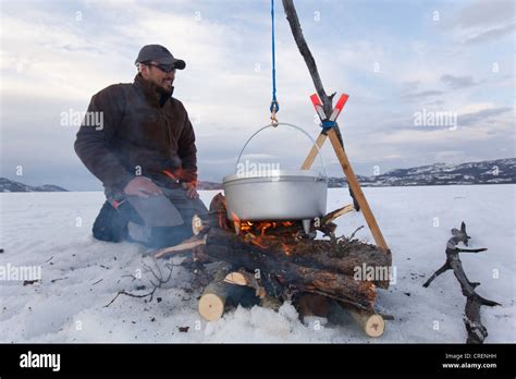 Man Cooking On A Camp Fire In A Hanging Dutch Oven Ice Of Frozen Lake