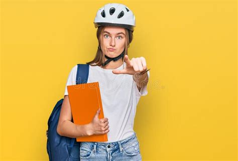Beautiful Young Blonde Woman Wearing Backpack And Bike Helmet Pointing With Finger To The Camera