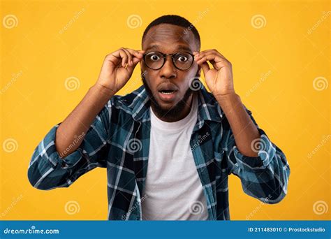 Amazed Black Man Looking At Camera Through Glasses Yellow Background