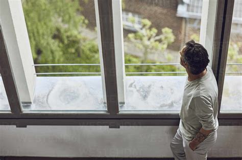 Senior Man Looking Out Of Window In A Loft Flat Stock Photo