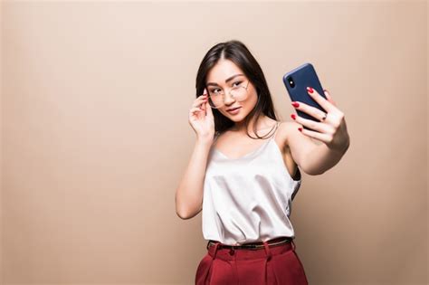 La Muchacha Bastante Asiática Toma El Selfie Con Su Teléfono Inteligente Aislado En La Pared
