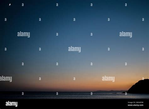 A mysterious dusk unfolds as the moon rises over the tranquil sea