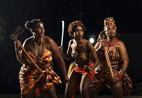 Three Women Dressed In African Style Clothing Holding Sticks And Wearing Headdress Standing
