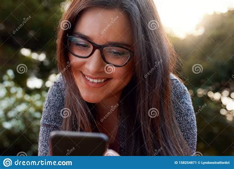 Close Up Of Smiling Young Woman Wearing Black Eyeglasses Using Smart Phone At Outdoors Stock