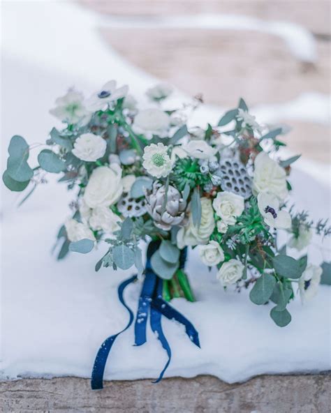 A Bridal Bouquet Sitting On Top Of A Snow Covered Bench With Blue