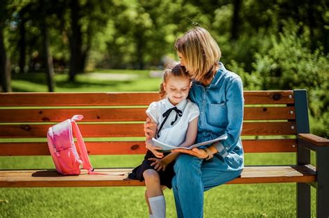 Мать и маленькая дочь в общественном парке на открытом воздухе сидя на скамейке и читать книгу