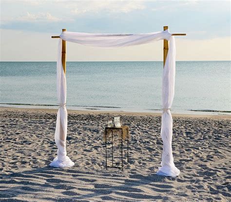 An Outdoor Wedding Setup On The Beach With White Draping And Wooden