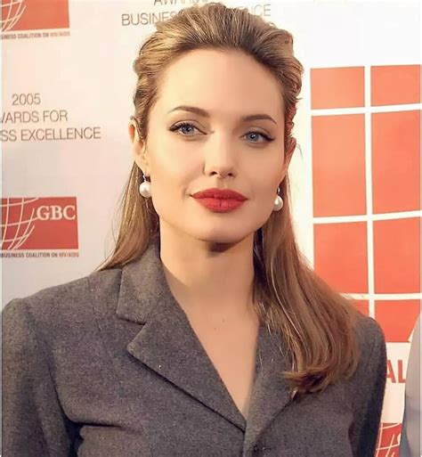 a woman with long hair wearing a gray suit and red lipstick is posing for the camera