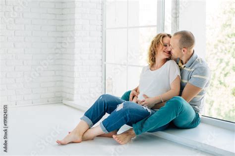 Young Happy Pregnant Couple In Love Barefoot Sitting On Windowsill
