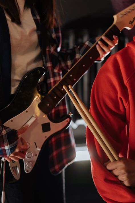 Close Up Shot Of Two Persons Holding An Electric Guitar And Drumsticks