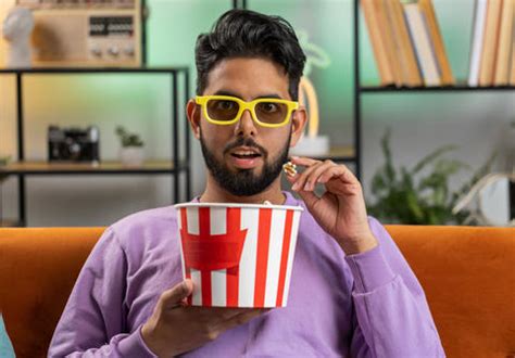 Indian Man Sits On Couch Eating Popcorn And Watching Interesting Tv