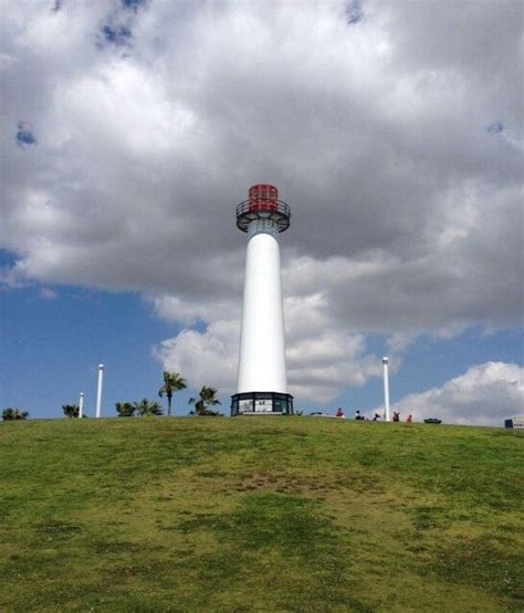 A Large White Light House Sitting On Top Of A Lush Green Hillside Under