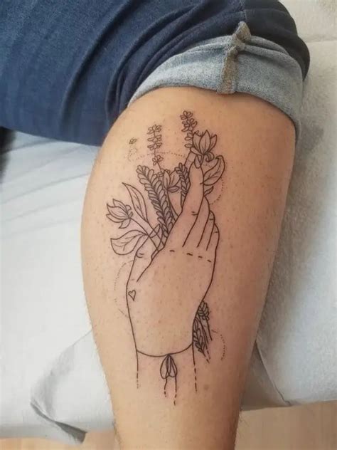 A Tattoo On The Leg Of A Woman With Flowers In Her Hand And Leaves Growing Out Of It