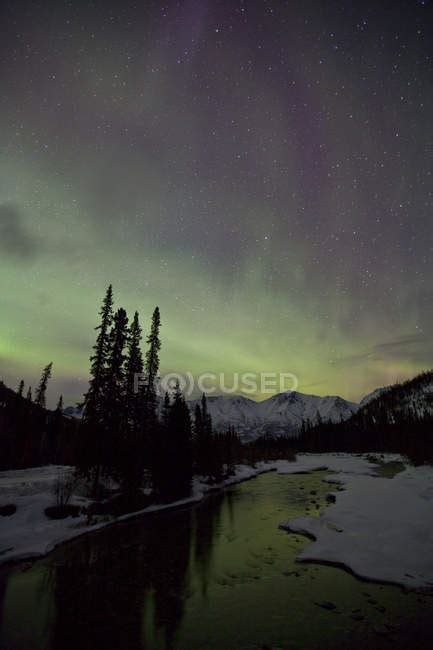 Northern Lights Above Mountains And Wheaton River Outside Of Whitehorse