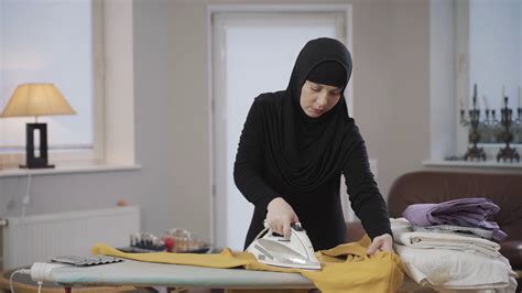 Portrait Of Concentrated Muslim Woman In Hijab Ironing Yellow Pullover