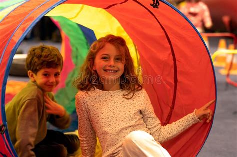 Cheerful Siblings Play Together On A Colorful Tube In The Playroom