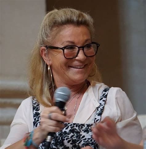 A Woman With Glasses Is Holding A Microphone And Smiling At The Camera