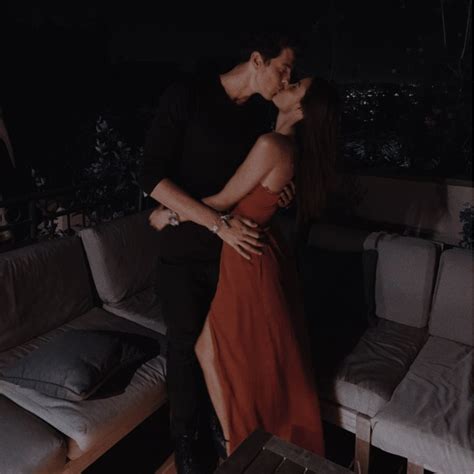 A Man And Woman Kissing In Front Of A Couch With The Lights On At Night