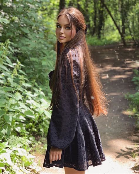 A Woman With Long Hair Is Standing In The Woods Wearing A Black Dress