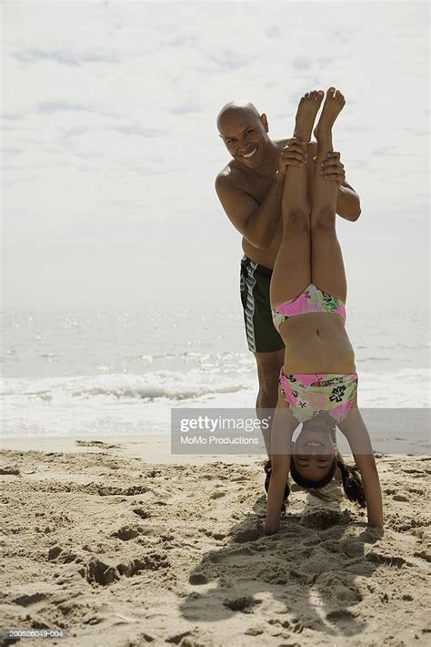 Father Helping Daughter Balance Upside Down At Beach Photo Getty Images