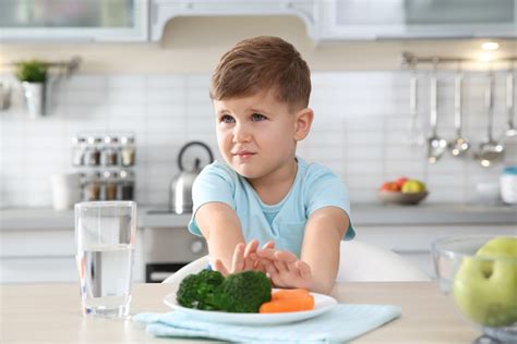 Adorable Little Boy Refusing To Eat Vegetables At Table In Kitch