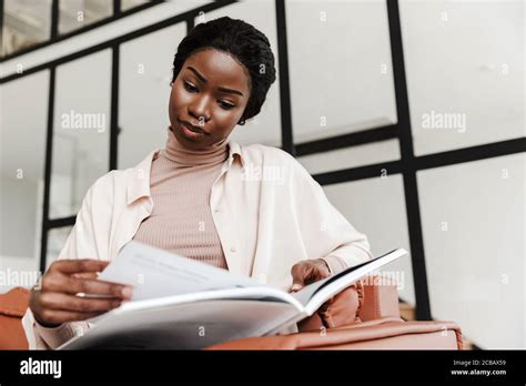 Photo Of Pretty Concentrated Young African Woman Sitting On Sofa Indoors At Home While Reading