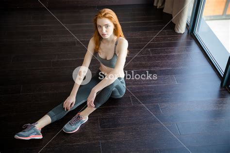Portrait Of A Fitness Redhead Woman Sitting On The Floor And Looking At