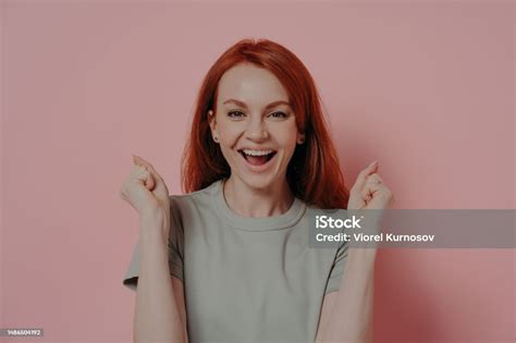 Young Overjoyed Redhead Woman Raising Hands Up With Clenched Fists Doing Champion Gesture Stock