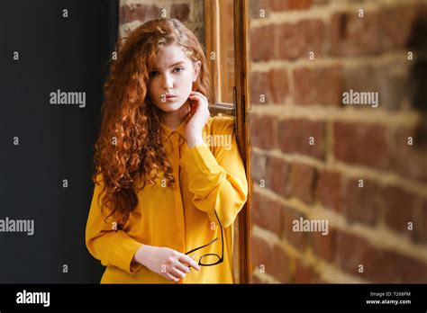 Curly Redhead Girl In The Yellow Shirt Standing With Glasses Near The